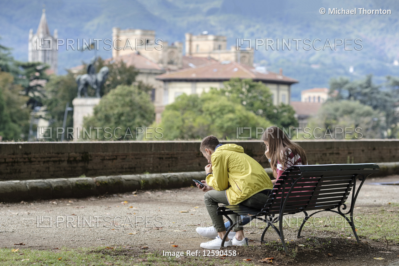 Young couple using smartphones relaxing on top of the ancient city wall of ...
