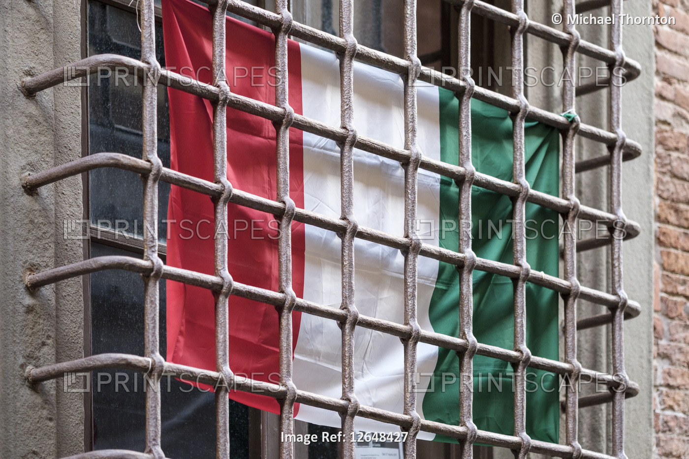 Italian flag behind window security bars, old city street in Lucca, Tuscany, ...