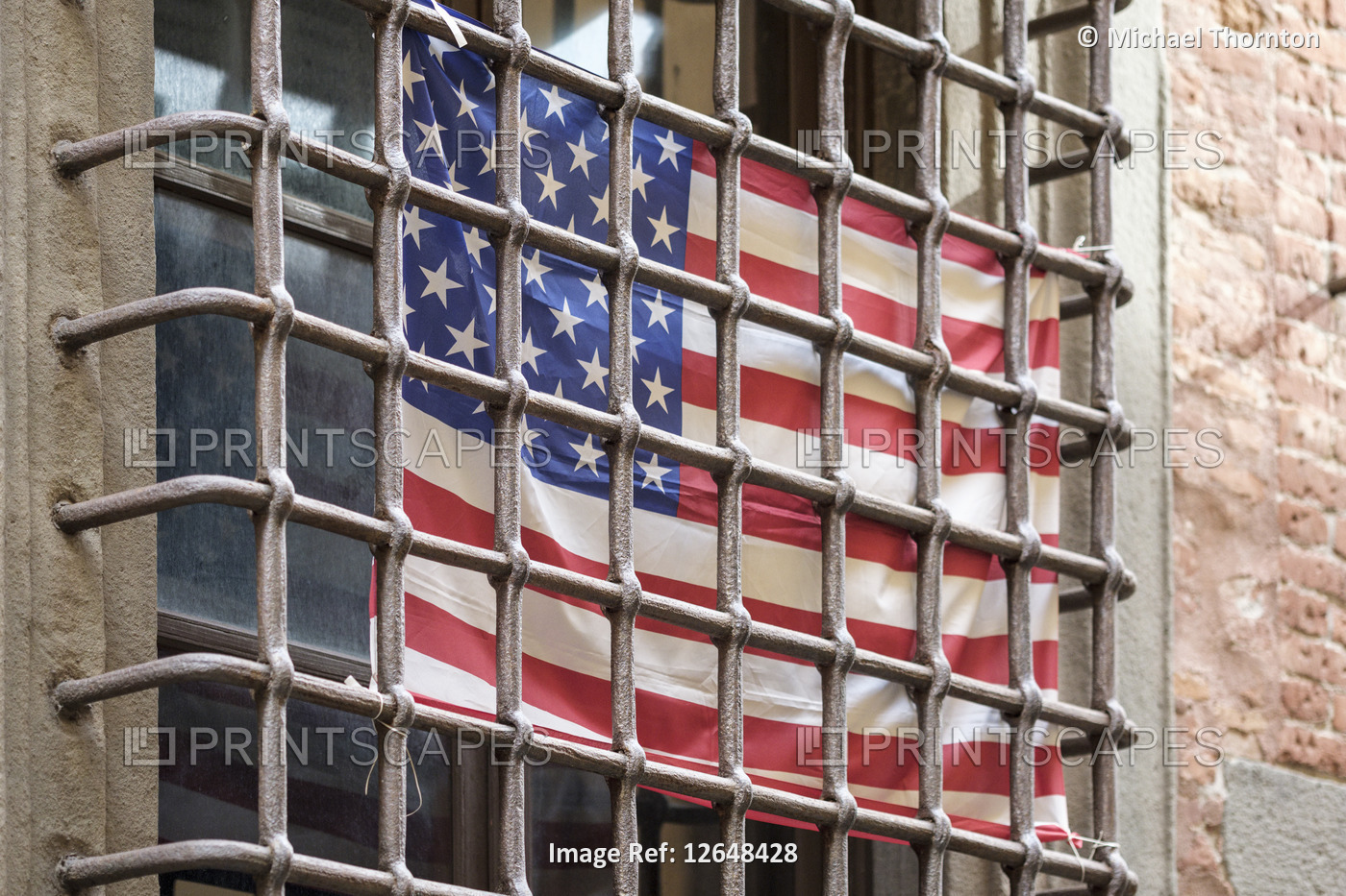 American flag behind window security bars, old city street in Lucca, Tuscany, ...