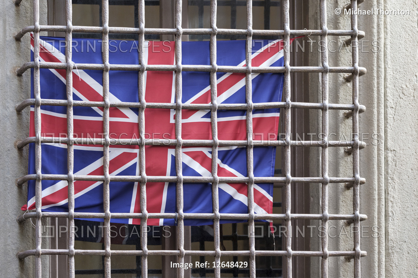 British flag behind window security bars, old city street in Lucca, Tuscany, ...