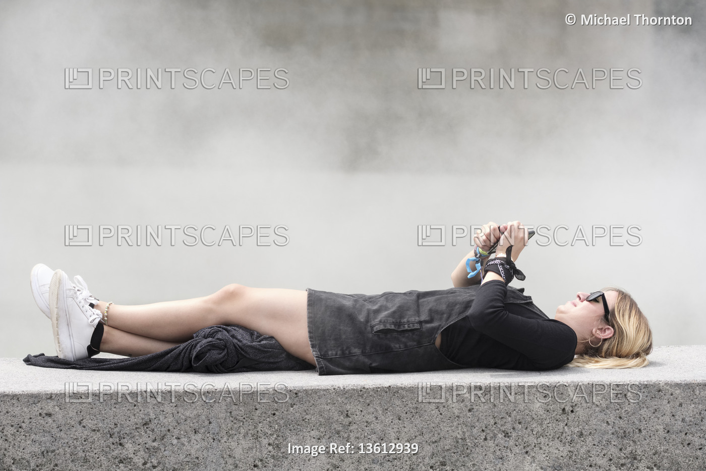 Young blonde lady with Ponytail, lying on wall with mobile phone, Bilbao, ...