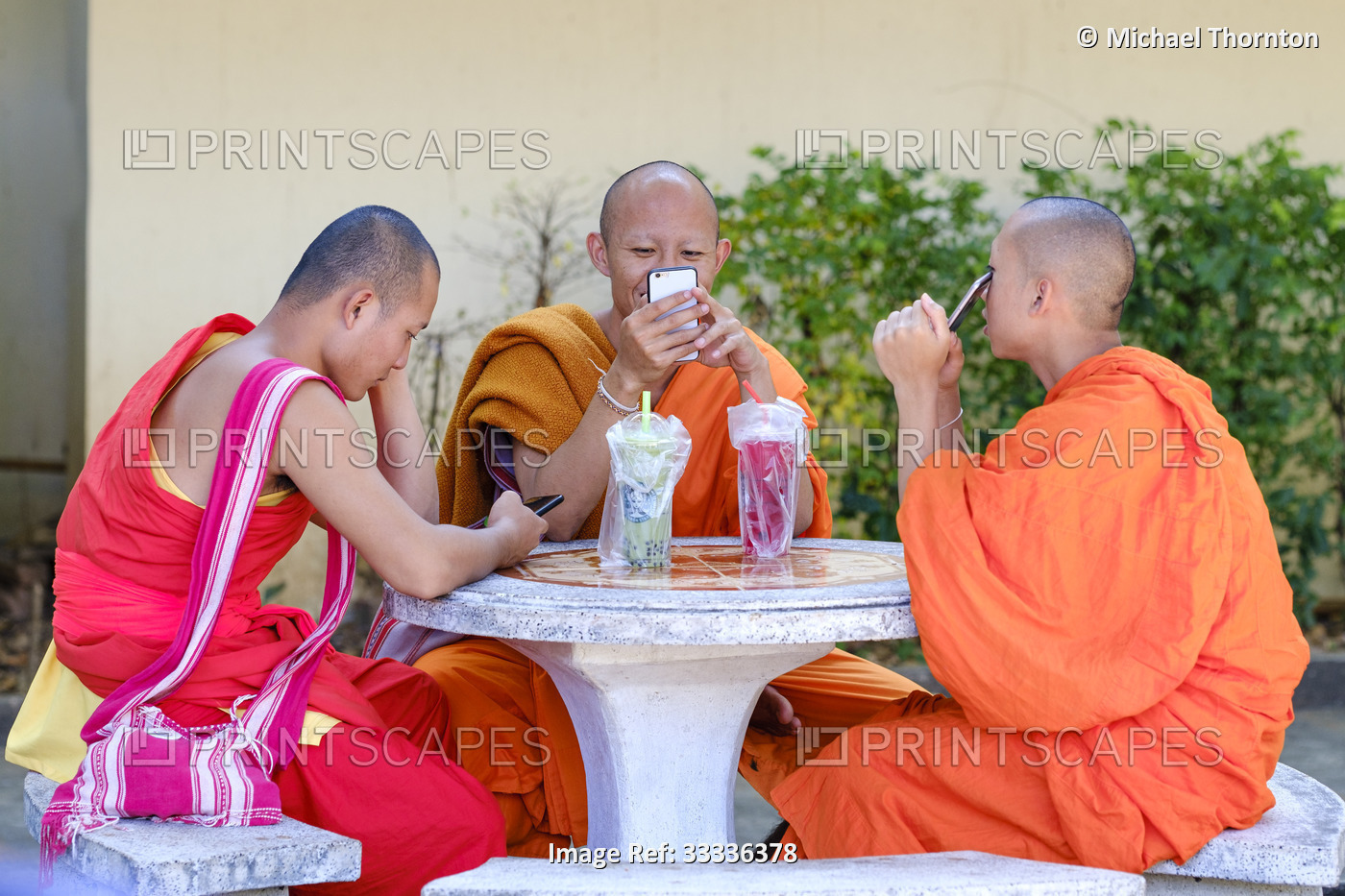 Three monks with smartphones relaxing at table with drinks, Wat Suandok, Chiang ...